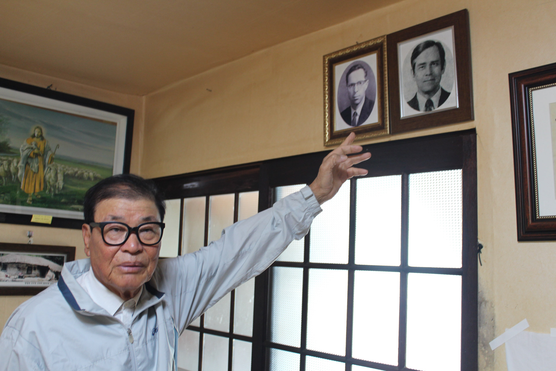 Man points to two framed photo pics at wall