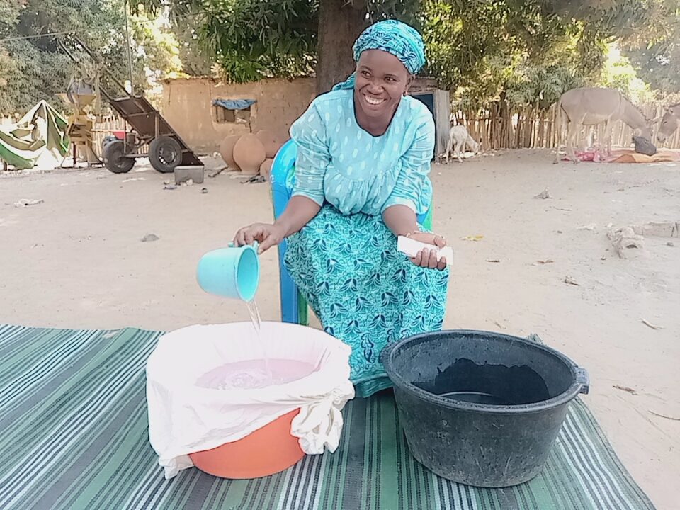 A woman filters water into a basin while holding treatment tablets.