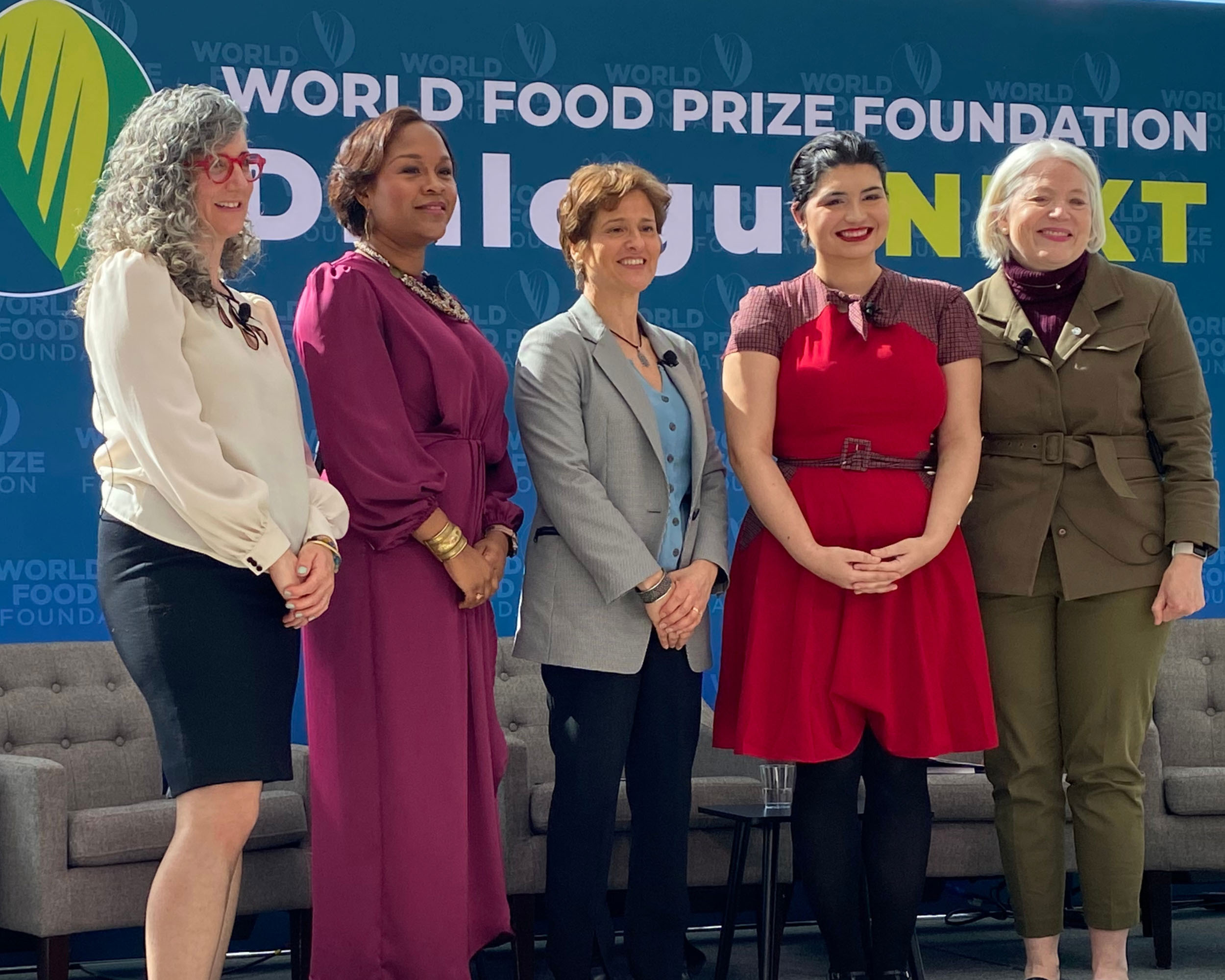 A group of six individuals pose for a photo on a stage at an event.