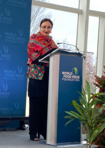A woman speaks at a podium in an event space with natural lighting.