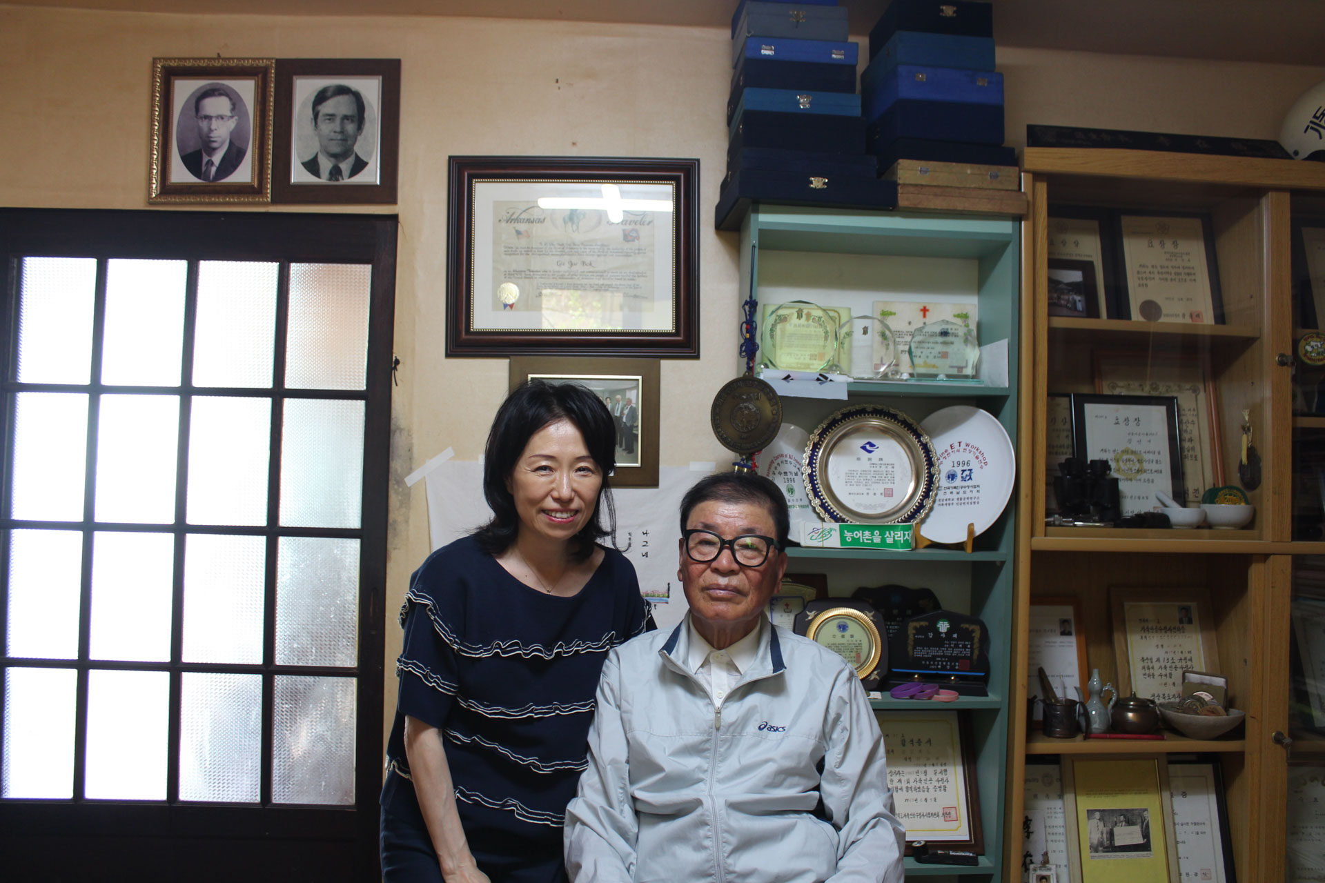 A man and woman pose together in a room filled with awards.