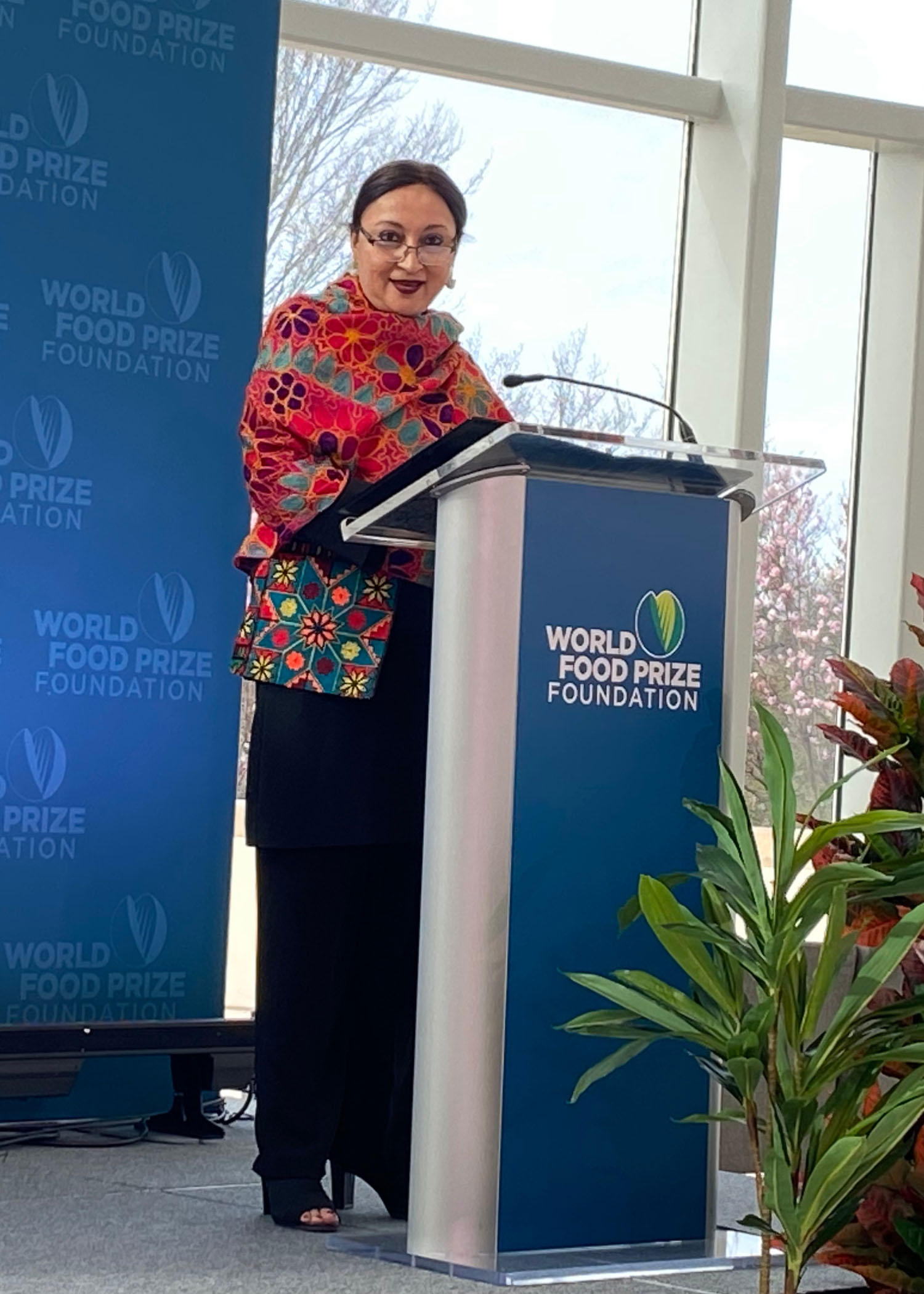 A woman speaks at a podium in an event space with natural lighting.