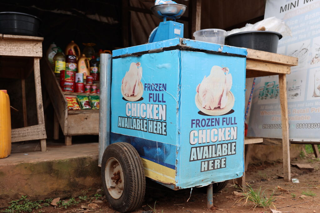 A mobile cart displays frozen chicken for sale outside a small shop.