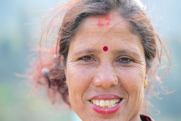 A close-up portrait of a smiling woman with a red bindi on her forehead.