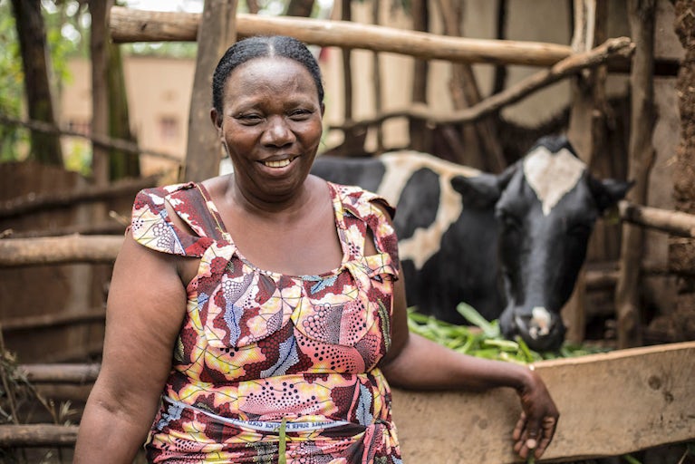 A woman standing by a fence with a cow in the background.