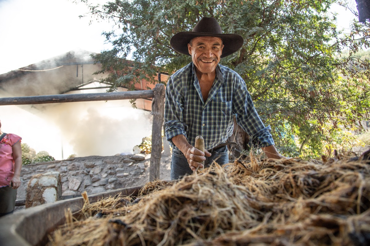 A man uses a stick to stir a pot of pulp as he smiles at the camera.