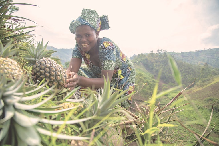 Woman in patterned dress smiling while harvesting pineapples on a hillside.