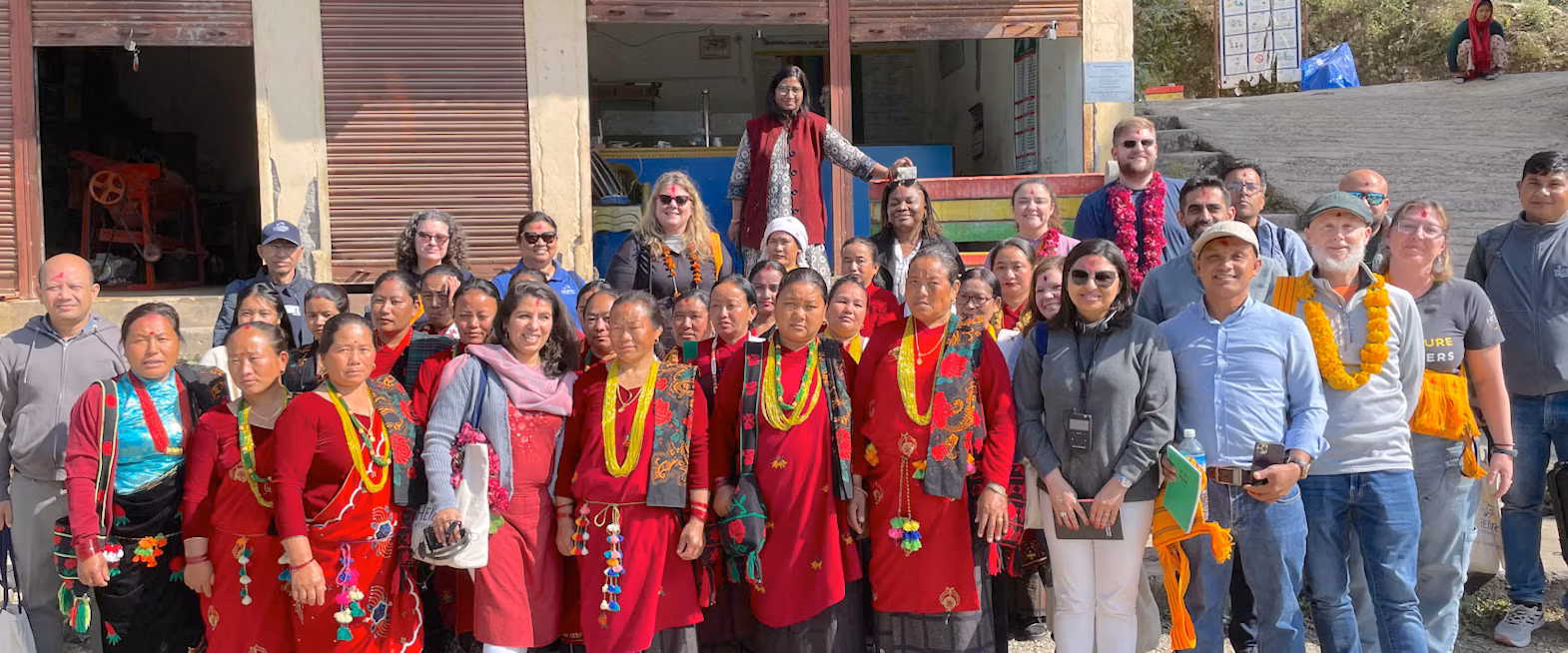 A large group of members of Atipriya Women’s Cooperative welcome visitors with traditional attire and garlands in Nepal.