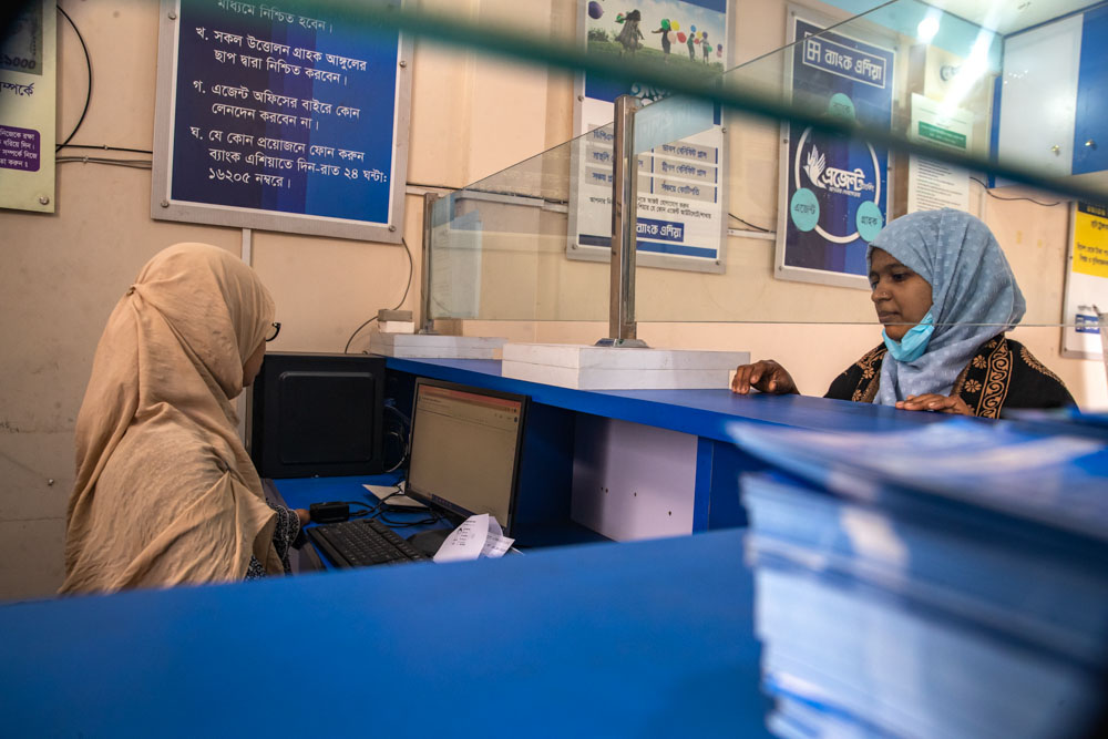 A woman stands at the desk of a bank teller in Bangladesh.