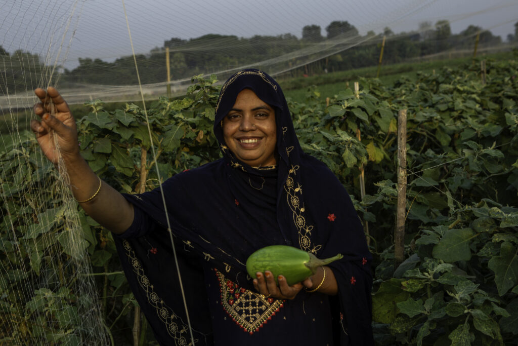 A woman holds an eggplant in a vegetable field in Bangladesh.