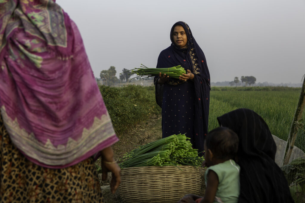 A woman farmer speaks with a group of women beside a vegetable field in Bangladesh.