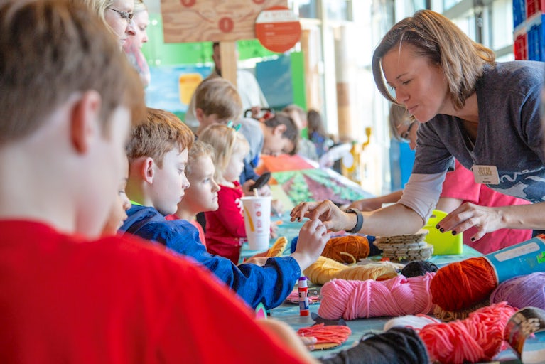 Volunteer helping a child with a craft at an event with other children.