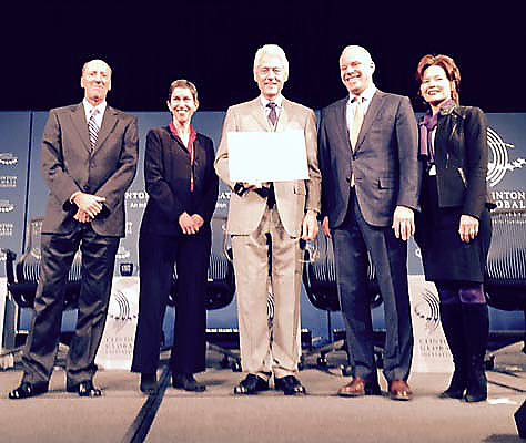 Group of five people in formal attire standing on stage with one person holding a certificate.