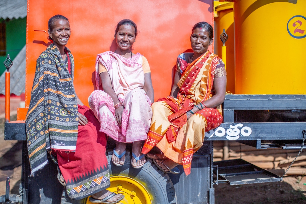 Left to right: Janaki Pangi, Damyanti Pangi and Sumitra Pangi pose on a large machine that is used to process turmeric that was donated by Passing Gifts. Previously the process took weeks, but now can be done in just a couple days.