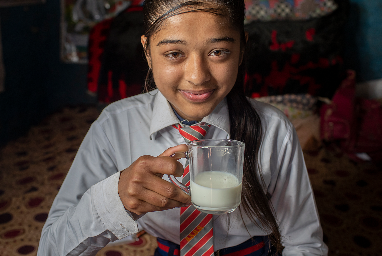 A young girl sips a glass of milk.