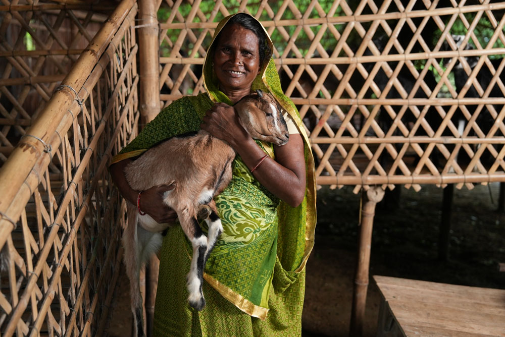 An Indian woman smiles for the camera holding a goat.