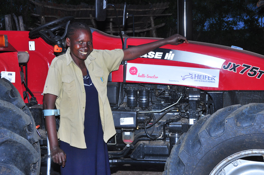 A woman stands in front of her tractor.