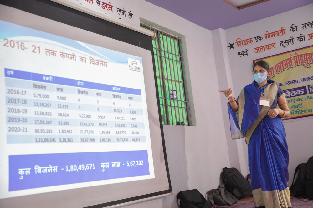 An Indian woman gives a presentation, gesturing at a screen displaying figures.
