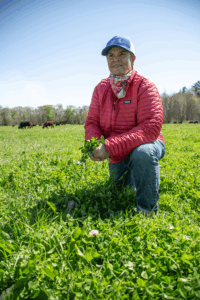 A rancher kneels in a field, holding crops in her hands.