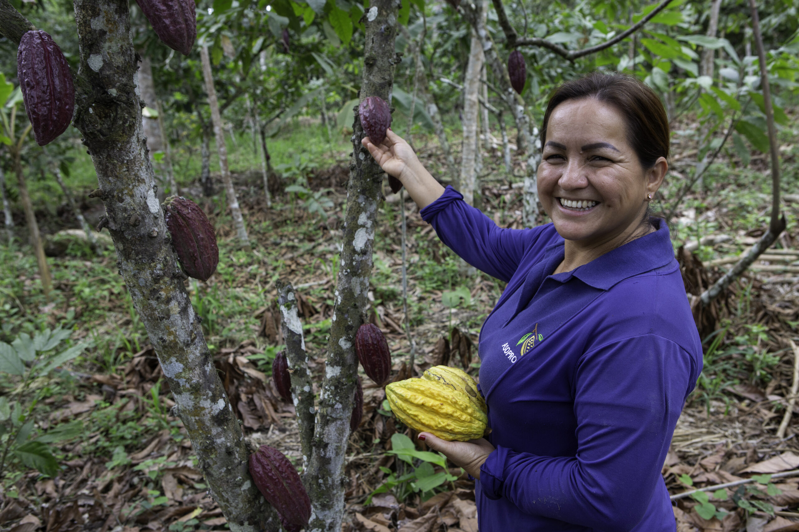 A woman smiles while holding a yellow cacao pod.