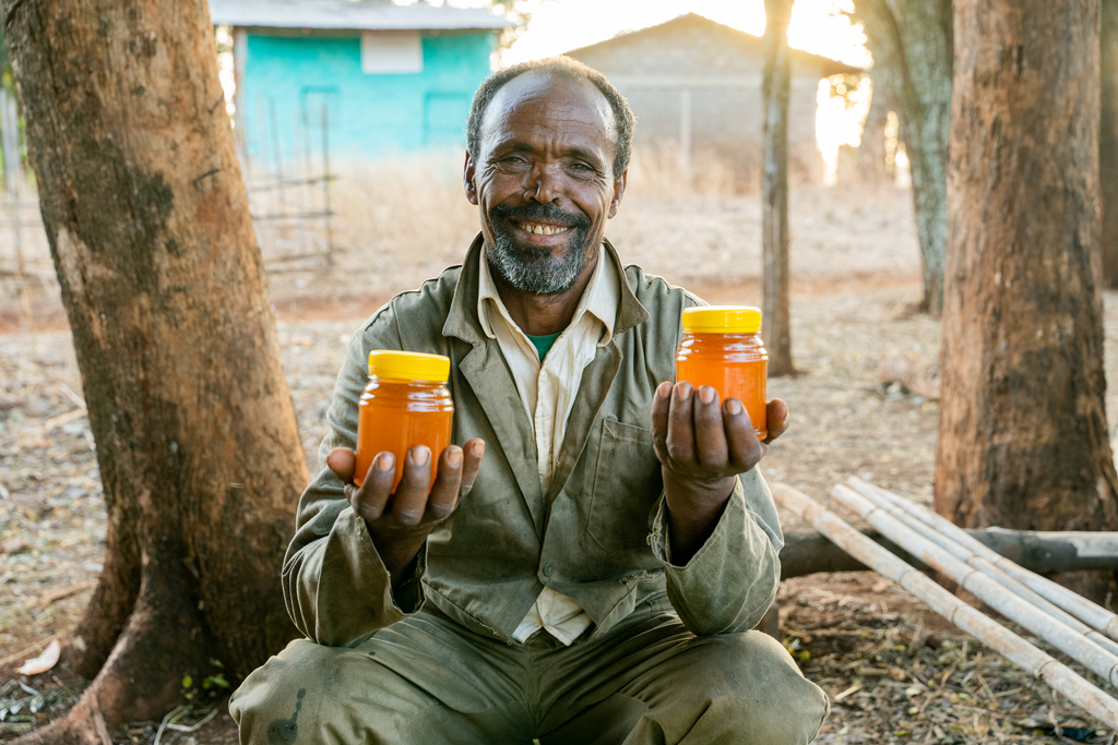 An Ethiopian man smiling and holding a jar of honey in each hand.