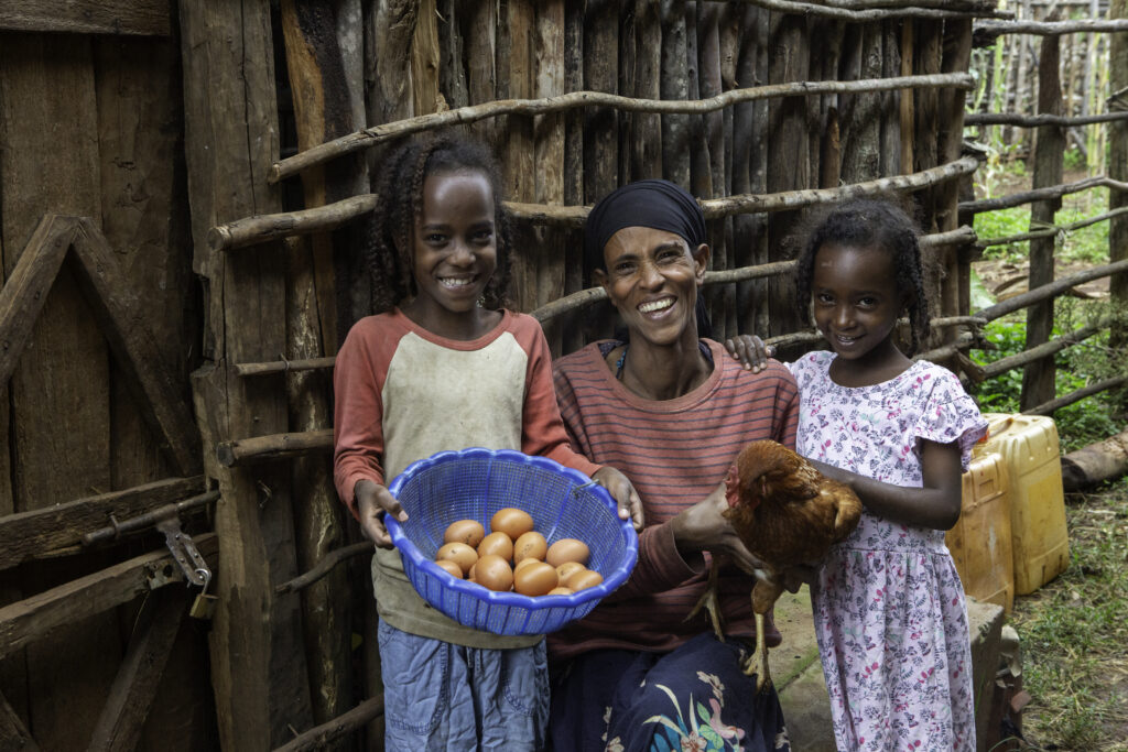 A woman smiles between her daughters holding a basket of brown eggs.