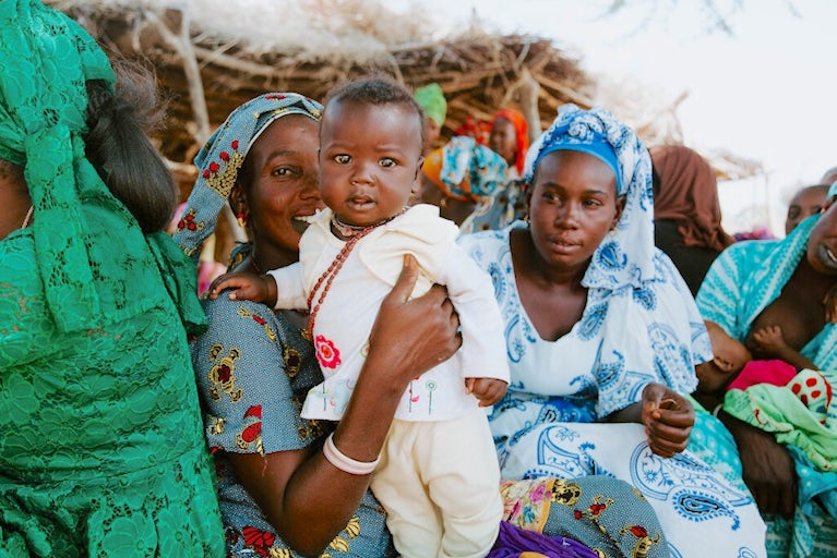 A woman holding a child, surrounded by other women.