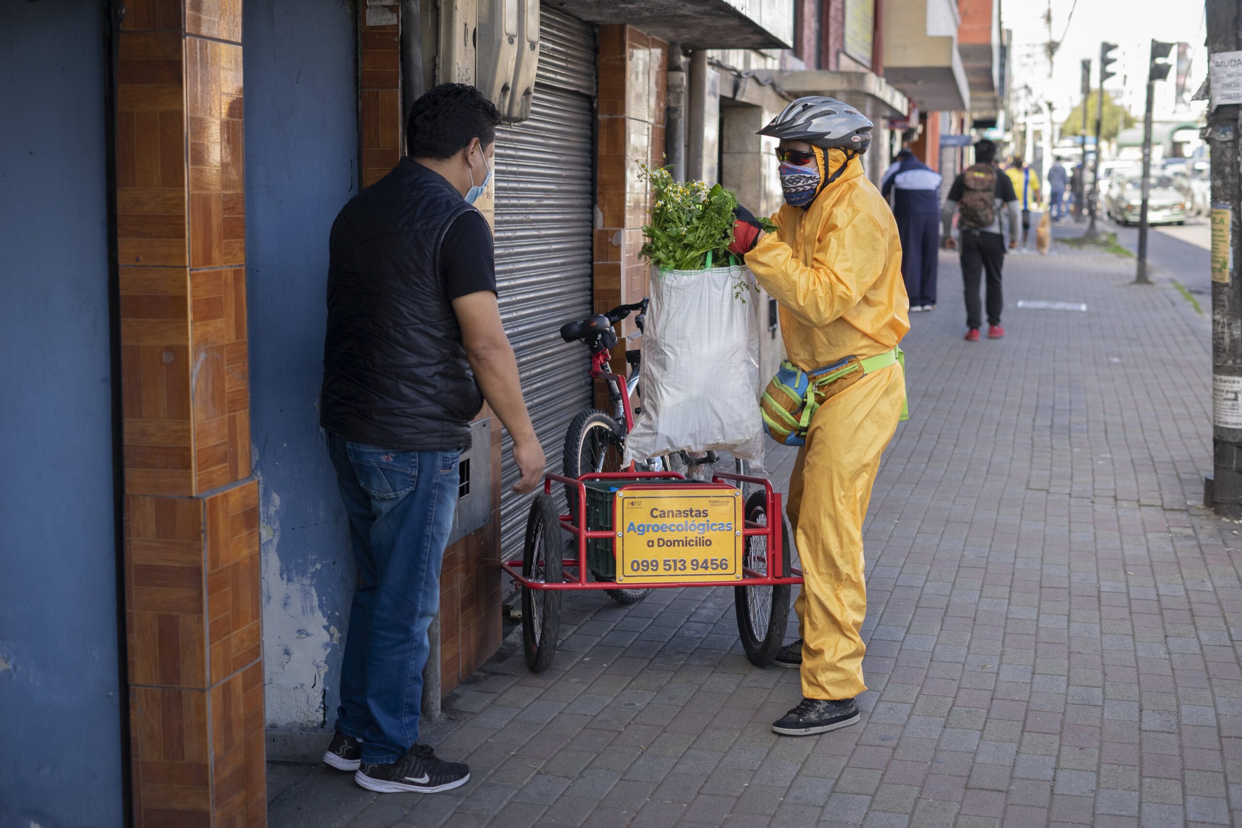 A man in protective gear hands a basket of food to another man.