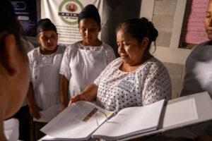 A woman reviews documents while surrounded by attentive female colleagues.