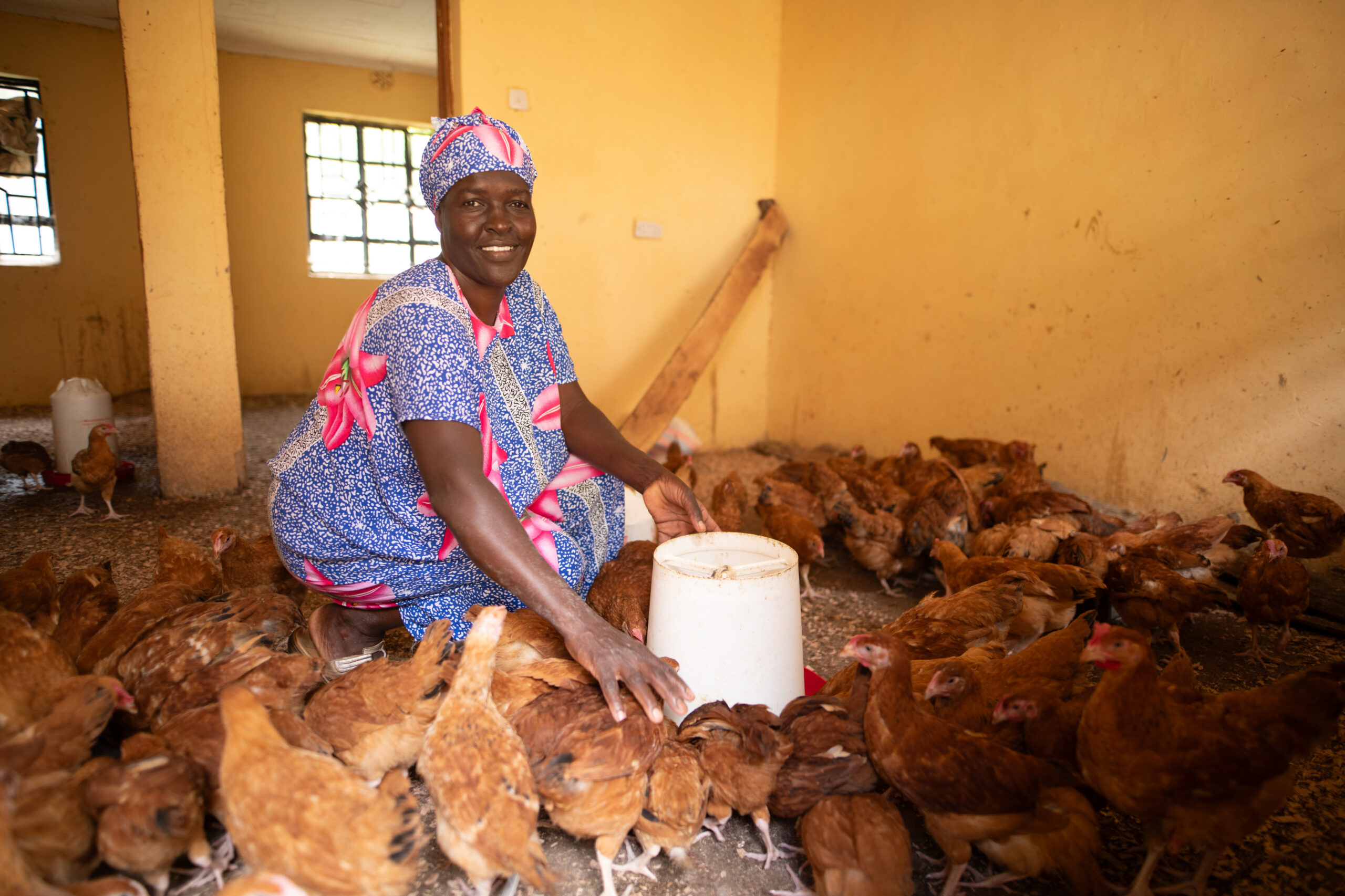 Woman smiles as she tends a flock of chickens inside a coop.