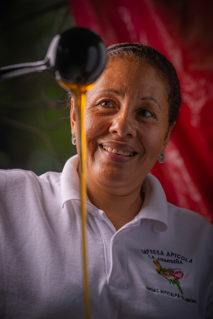 A Honduran woman pouring honey from a spoon in a long stream.