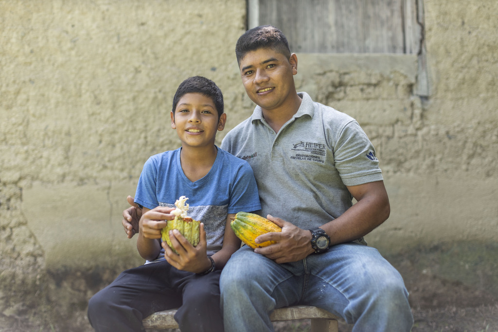 Brayan Ortiz and his father, Merlin, sit and smile together while Brayan eats cacao.