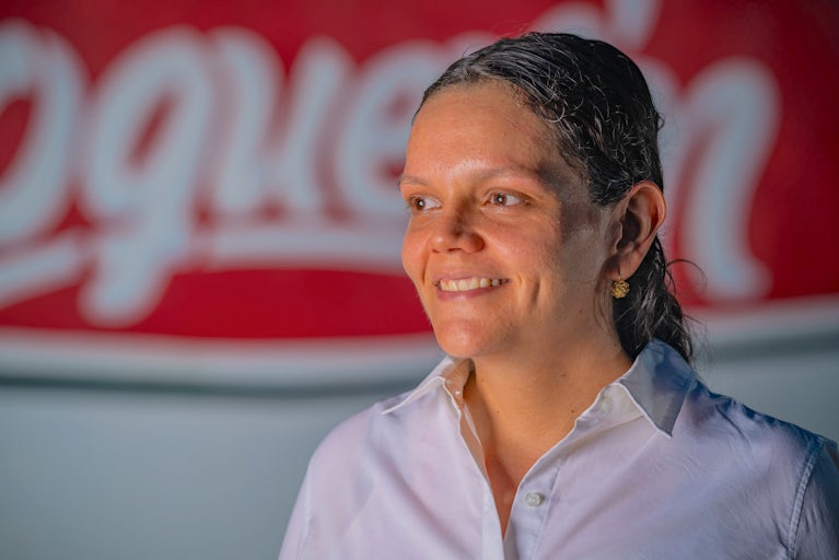 A woman in a white button-down shirt stands in front of a red and white sign.
