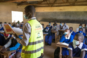 A man wearing a Hatching Hope vest teaches the benefits of eggs to a classroom of kids.
