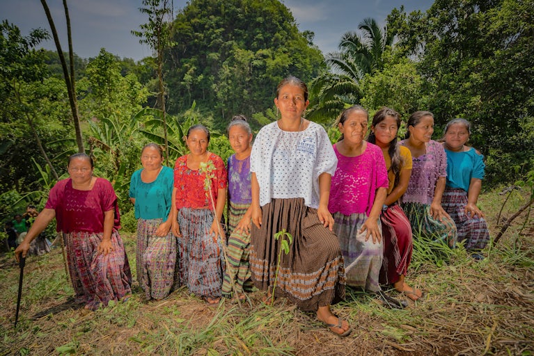 Group of women in colorful traditional clothing standing in a forested area.