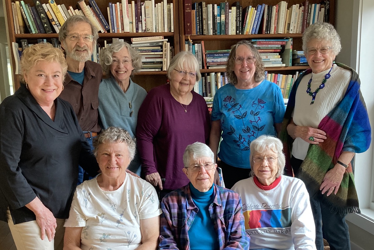 Nine adults pose in front of a bookshelf filled with books.