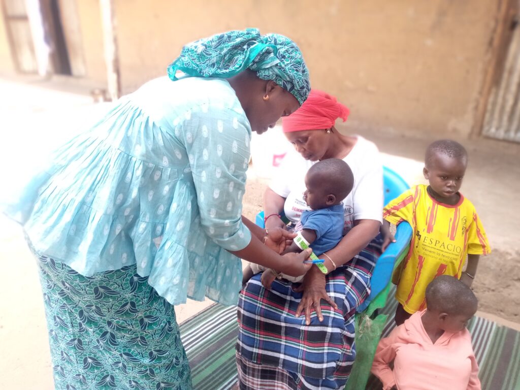 A woman in a blue dress measures a child’s arm while speaking with the child’s mother.