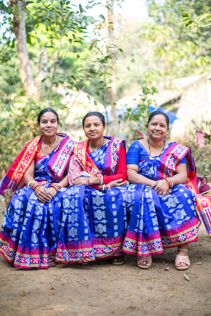 Three women sit together at a goat market in Odisha, India.