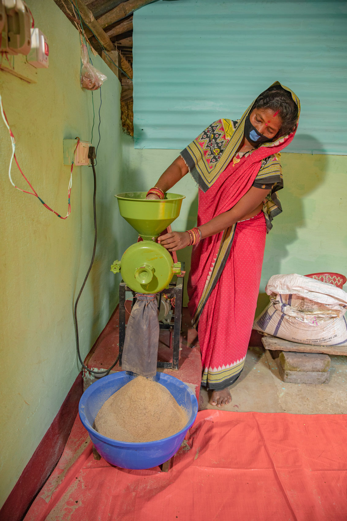 A woman pours chicken feed into a small mill. 