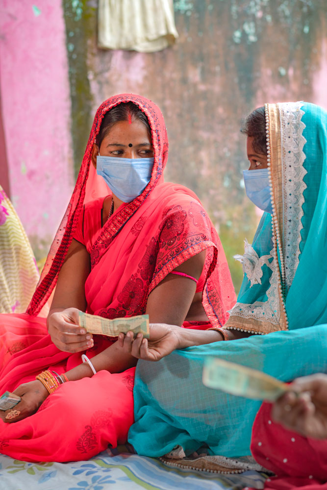 Two women in India exchange money as part of a group savings exercise.