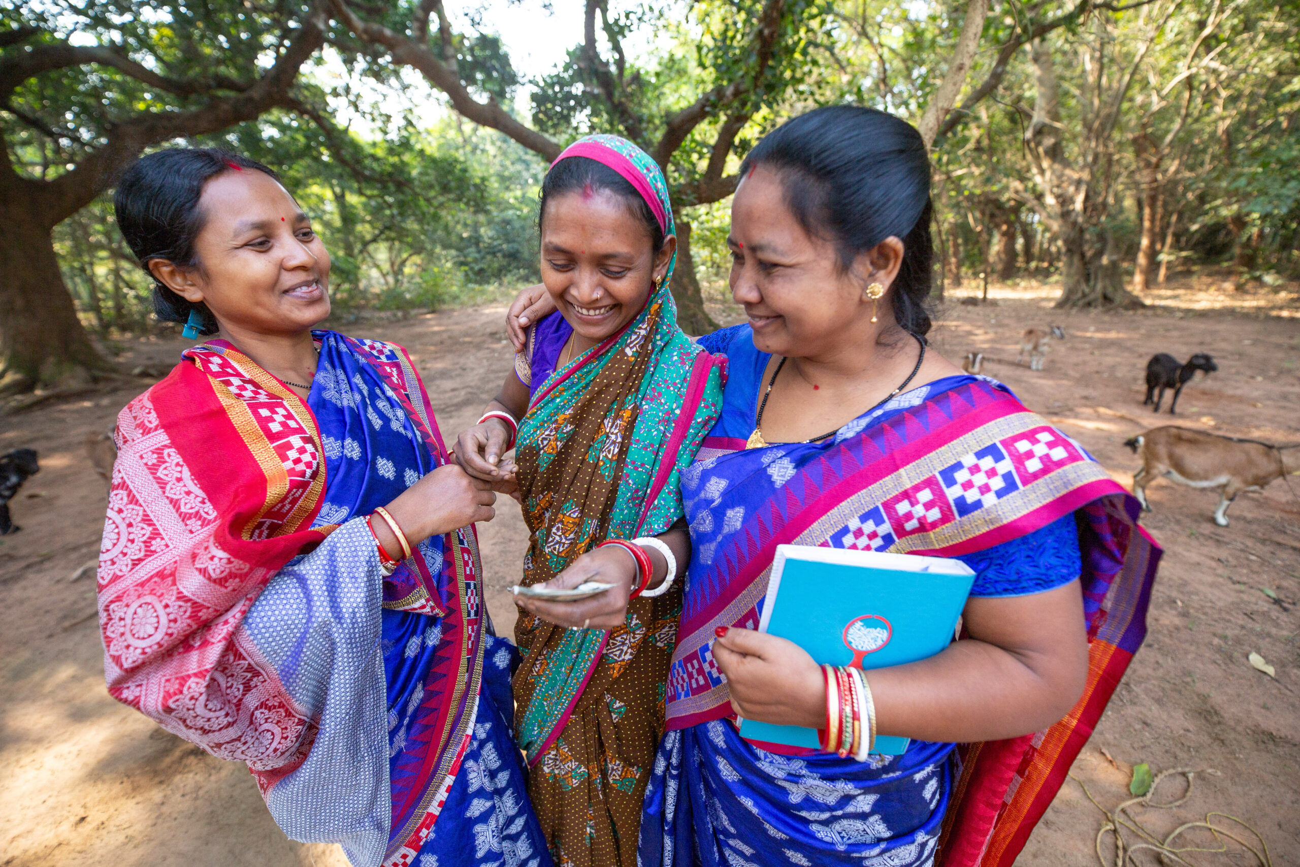 Three women hold cash outdoors in Odisha, India.