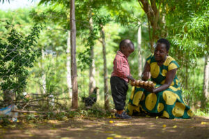 A woman in Kenya holds a carton of eggs out towards a small boy.