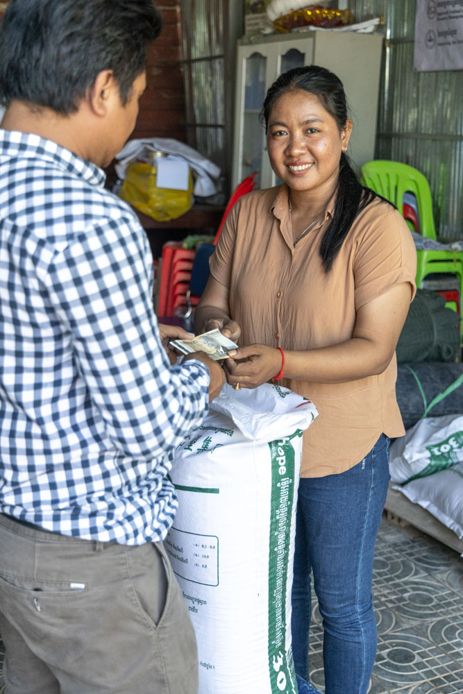 A woman in a light brown blouse exchanges money with a man.