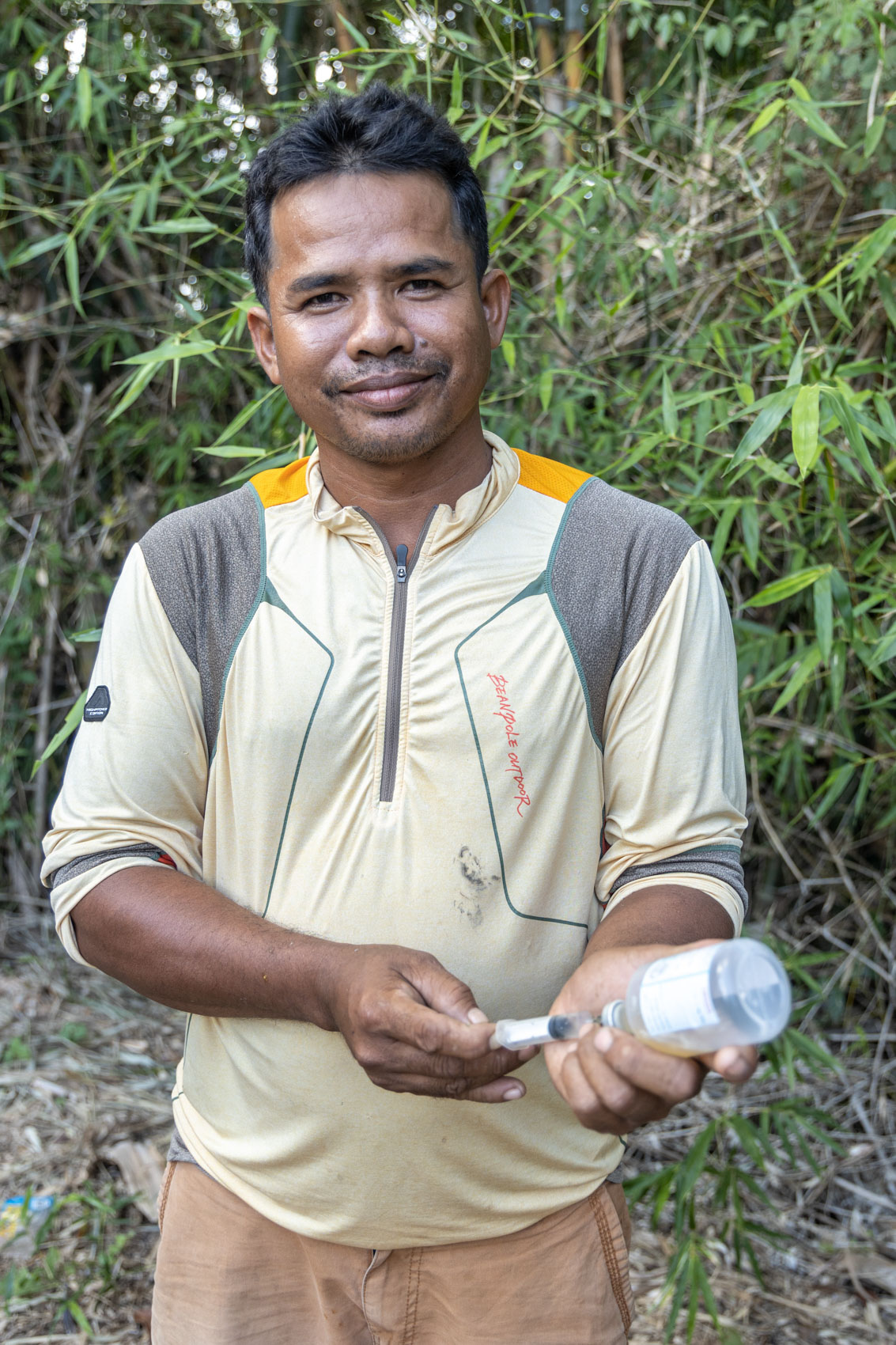 A man holds a syringe and vaccine vial while standing in a rural setting.