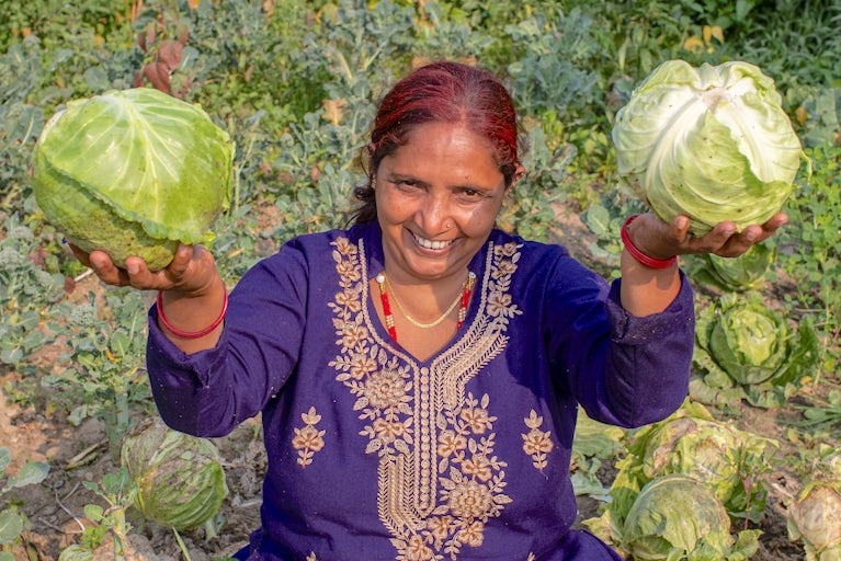 Smiling woman holding up cabbages.