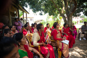 Group of women sitting outdoors under trees during a meeting.