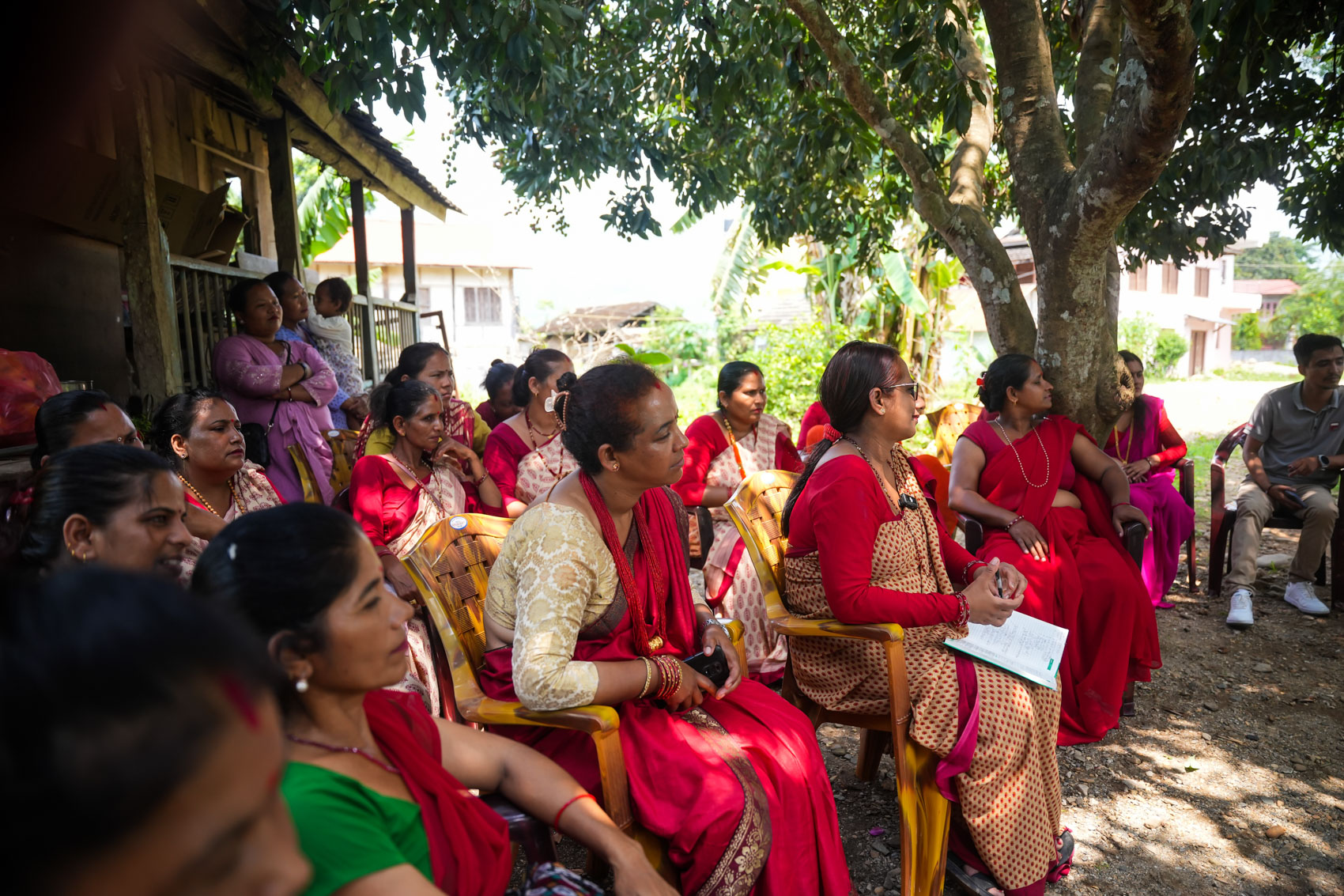 Group of women sitting outdoors under trees during a meeting.