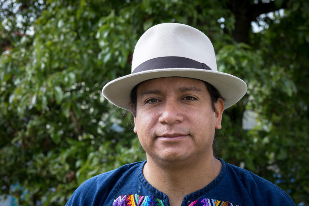 A man wearing a hat and blue shirt stares at the camera.