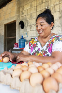 A woman sits at a table with several crates of eggs in front of her.