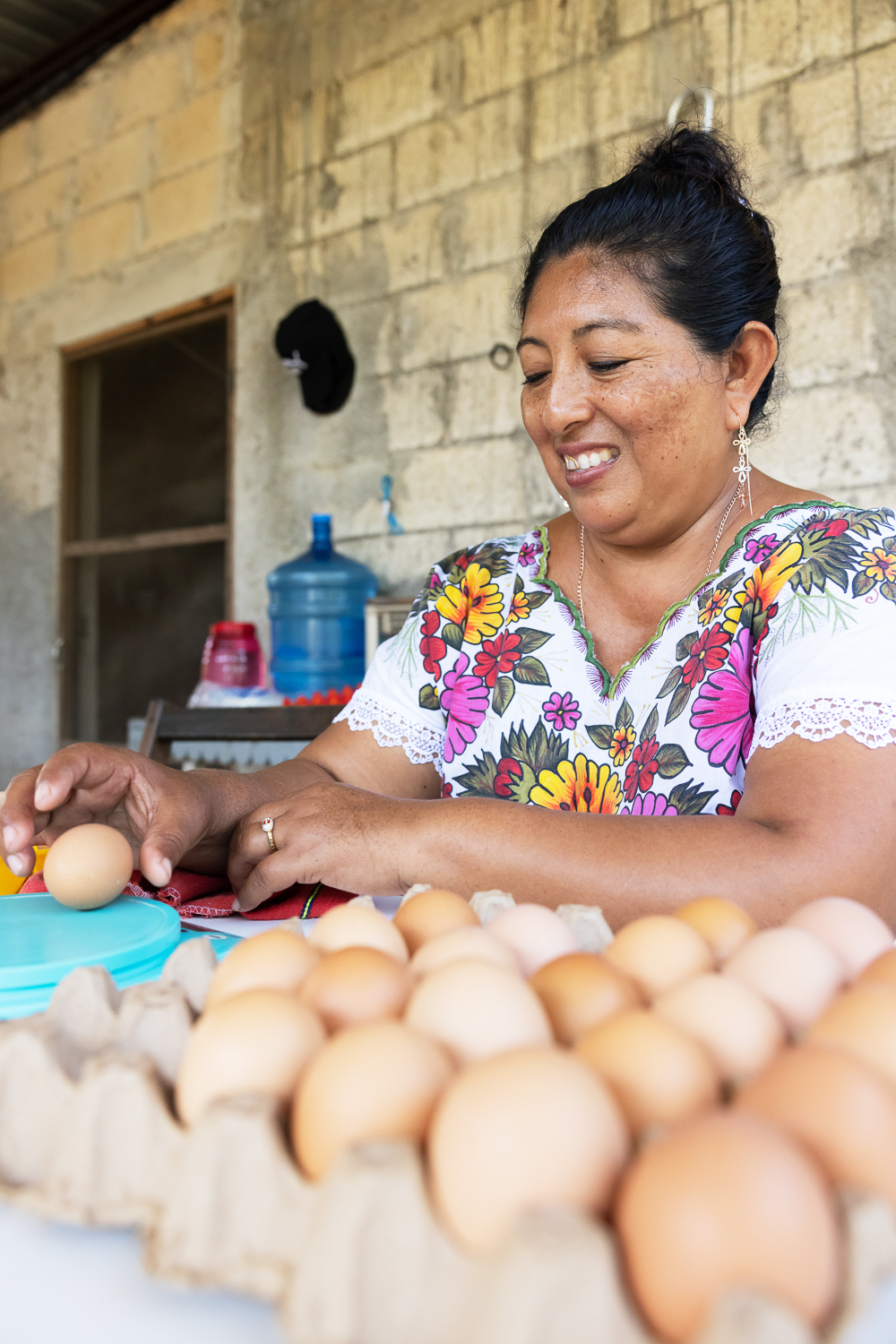 A woman sits at a table with several crates of eggs in front of her.